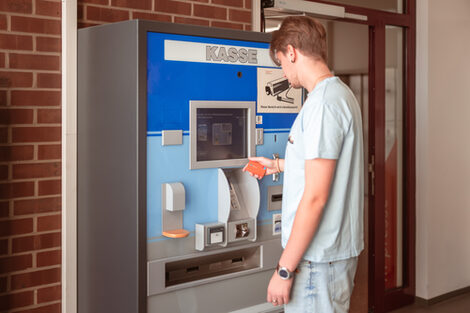 Photo of a young man operating the ticket machine in front of the library.