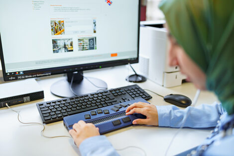 Photo of the hands of a visually impaired student placed on the Braille display in front of a computer screen.