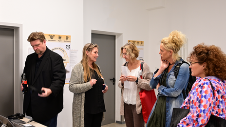 Diskussionsrunde aus vier Personen. Eine fünfte Person schaut sich den Formulargenerator an.