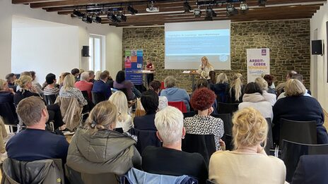 Standing at a table, Ansgar Rahmacher, Marcel Mitas and Leon Sachweh present assistance systems for the health and care sector.