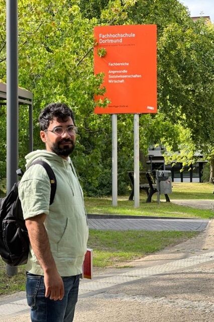 Am Projekt beteiligter Student des FB 8 steht vor einem Schild der FH am Standort Emil-Figge-Straße