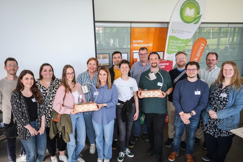 Eine Gruppe von Menschen, darunter die Preisträger:innen mit Pokalen in der Hand