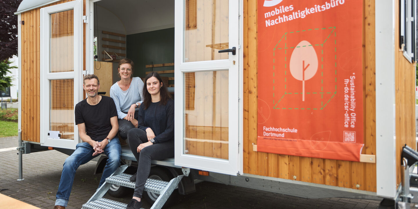 You can see 3 people sitting in a construction trailer, which you enter via a small staircase. There is a large poster attached to the trailer that reads "Soffi mobile sustainability office".