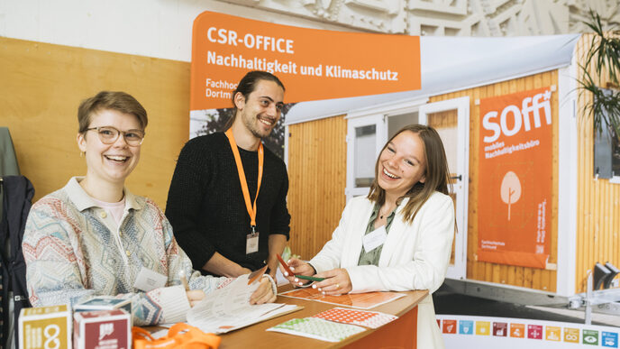 Three receptionists stand behind the counter and laugh amiably into the camera