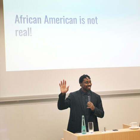 One person stands at the lectern, holds up his right hand and smiles towards the audience.