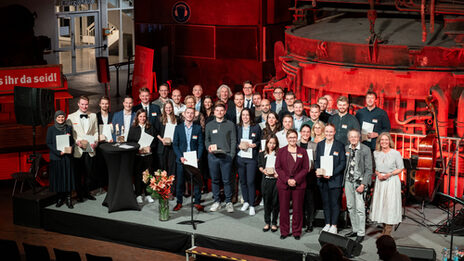 Many people stand on the stage in front of the blast furnace in the DASA steel hall.