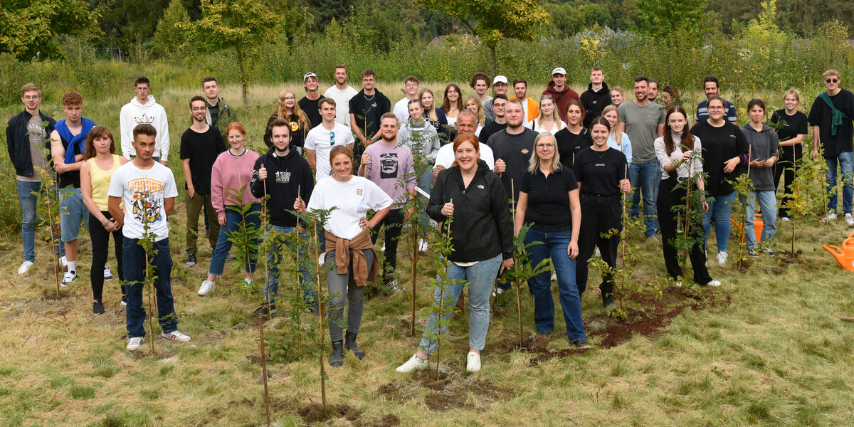 A group of people are standing in a field where small trees have been planted.