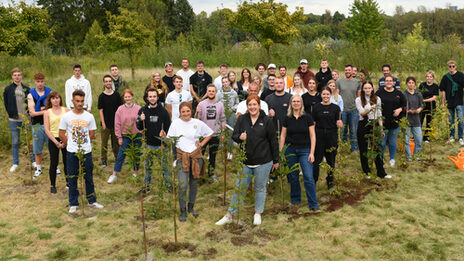 A group of people are standing in a field where small trees have been planted.