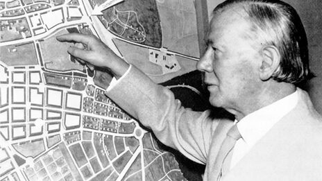 A male person stands in front of a city map and points to a square.