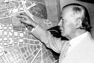 A male person stands in front of a city map and points to a square.