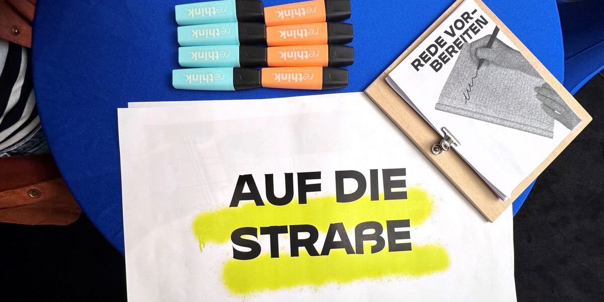 Auf einem Tisch liegt ein Plakatentwurf mit der Aufschrift "Auf die Straße".