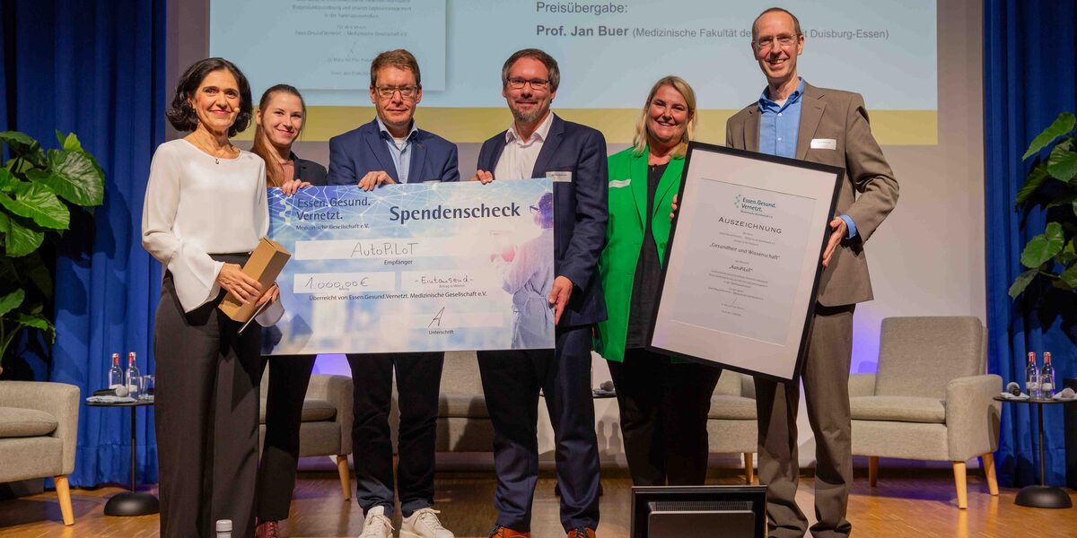 Six people stand next to each other on a stage. They present a large-format donation check and a certificate.