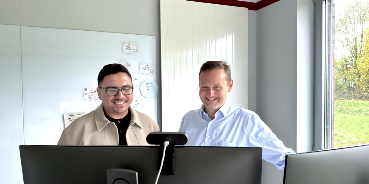 Zwei Personen stehen hinter zwei Monitoren und blicken darauf.