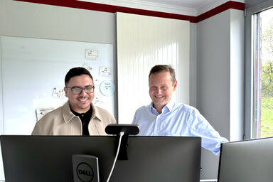 Zwei Personen stehen hinter zwei Monitoren und blicken darauf.