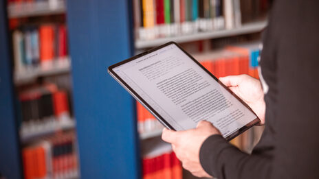 Photo of a tabelt in the hand of someone standing in a library.