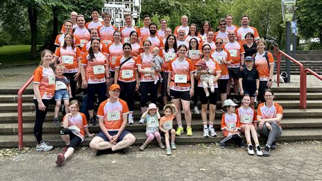 Several adults and children are standing and sitting on a staircase. Most of them are wearing a shirt with orange and white elements.