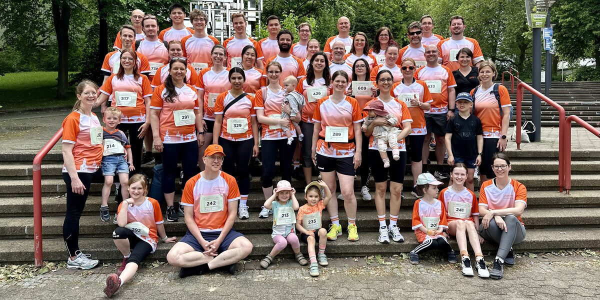 Several adults and children are standing and sitting on a staircase. Most of them are wearing a shirt with orange and white elements.