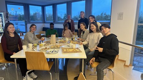 Several people are sitting at a table with cookies and coffee.
