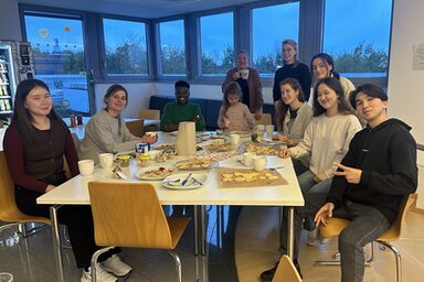 Mehrere Personen sitzen an einem Tisch mit Keksen und Kaffe.