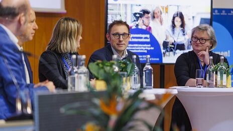 Vier Personen sitzen auf einer Bühne und sprechen miteinander in einer Diskussionsrunde.