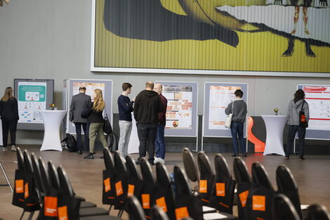 Chairs can be seen in the foreground. In the background, several participants look with interest at the posters of the doctoral students displayed on large pinboards.