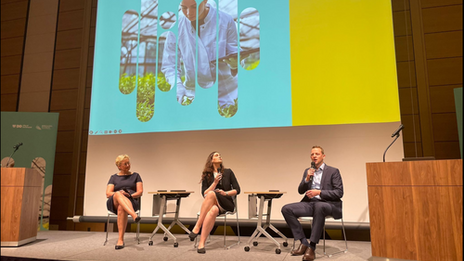 Drei Personen sitzen nebeneinander auf einer Bühne und halten jeweils ein Mikrofon.