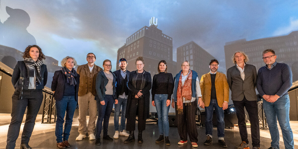 Group picture with 11 people standing next to each other in front of a projection showing the Dortmund U from the outside.