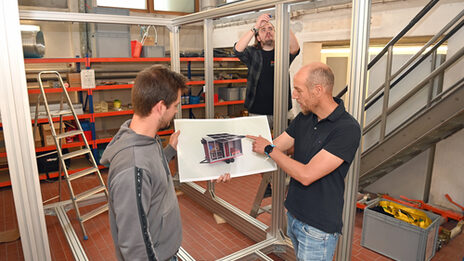 Drei Menschen stehen in einer Werksstatt