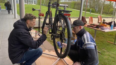 Two people are working on a bicycle at the FH Emil-Figge-Straße campus.