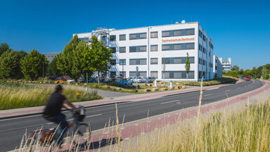 Gebäudeaufnahme mit Logoanbringung "Fachhochschule Dortmund" am Gebäude 38b - aus der Ferne. Fahrradfahrer fährt links ins Bild.