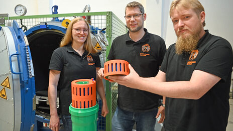 Three people stand in the high-voltage laboratory at Fachhochschule Dortmund and show a component of a battery storage system.