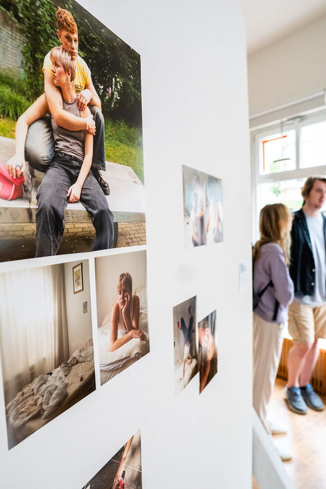 In the foreground, a series of pictures showing two queer friends. Guests chatting in the background.