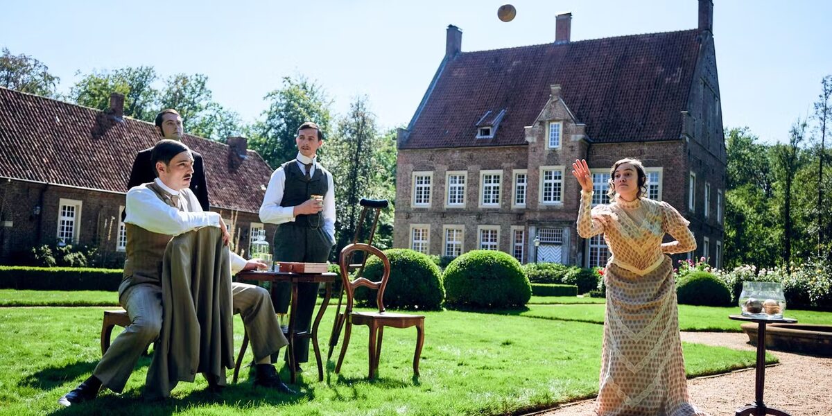 A woman throws a ball in front of a historic building. Three men watch her critically.