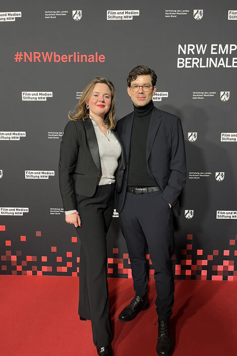 Zwei Personen stehen in schicker Abendgarderobe nebeneinander.