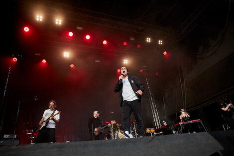 Eine männlich gelesene Person singt und tanzt auf einer Festivalbühne.