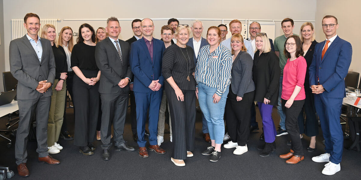 22 Personen stehen in einem Raum und blicken freundlich in die Kamera.