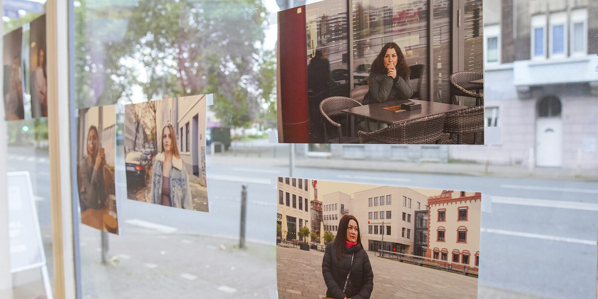 Auf einer Fensterscheibe sind mehrere Fotos angebracht. Die Fotos sind Teil der Ausstellung und zeigen die Gesichter geflüchteter Frauen, die jetzt in Deutschland leben.