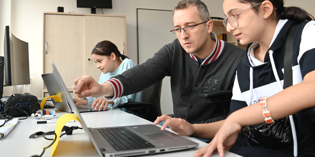 Three people are looking at notebook monitors. One person explains something.