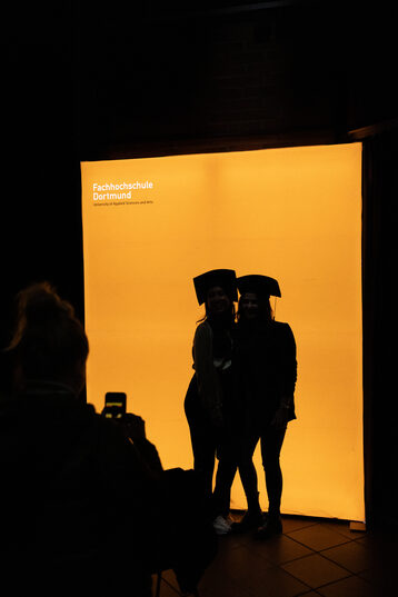 Two people backlit in front of a glowing orange wall.