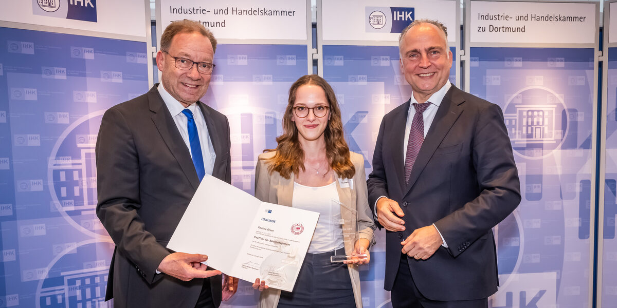 Three people stand next to each other at the presentation of an unfolded certificate and a transparent trophy.