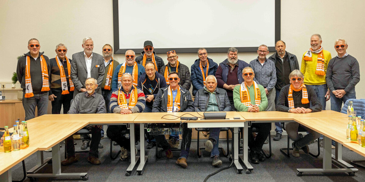 A large group of people in a seminar room. Many of them are wearing orange Fachhochschule Dortmund sunglasses.