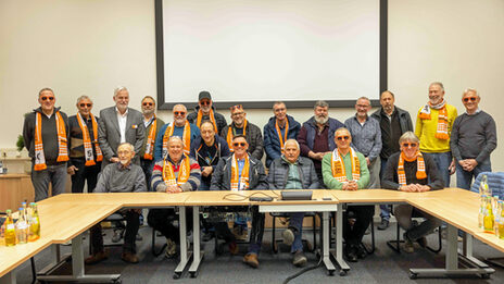 A large group of people in a seminar room. Many of them are wearing orange Fachhochschule Dortmund sunglasses.