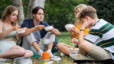 Vier Jugendliche sitzen auf einer Wiese uns essen aus Tellern.