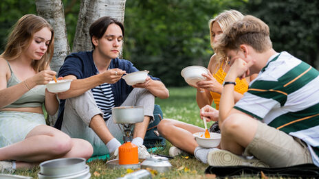 Vier Jugendliche sitzen auf einer Wiese uns essen aus Tellern.
