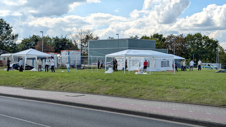 People set up pavilions and tents on a meadow.