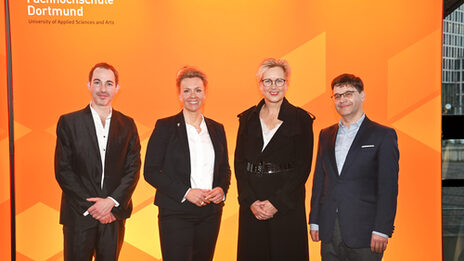 Four people stand next to each other in front of an orange UAS wall.