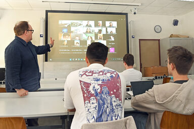 People sit in a seminar room and look at a screen on which other people are connected.
