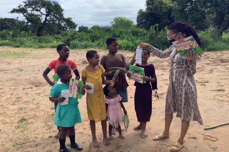 A social worker distributes the coloring book to a small group of children of different ages.