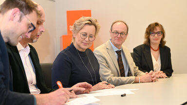 Several people are sitting at a table, signing papers.