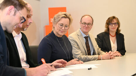 Several people are sitting at a table, signing papers.